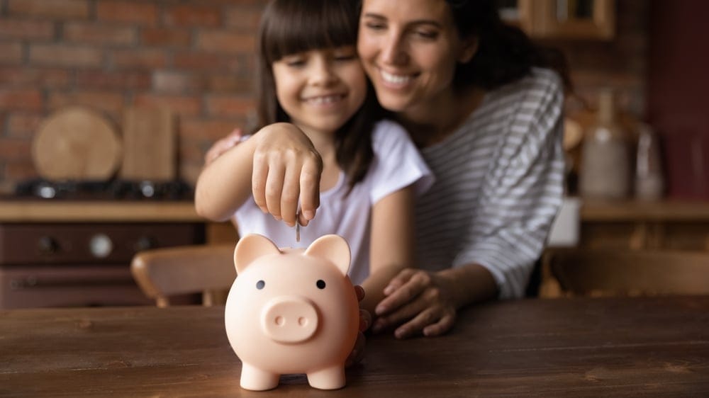 Woman with her daughter putting money in a piggybank.