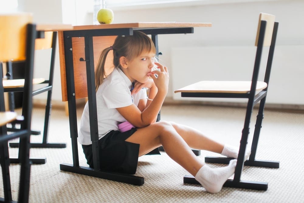 Little girl sitting under her desk.