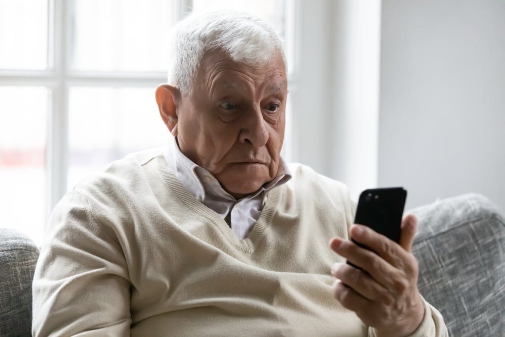 Old man on sofa befuddled by his phone.
