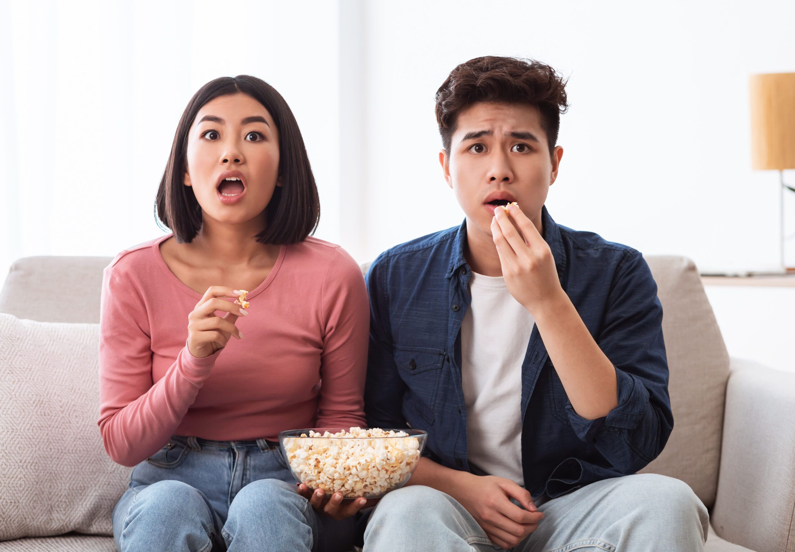Young couple eating popcorn at home.