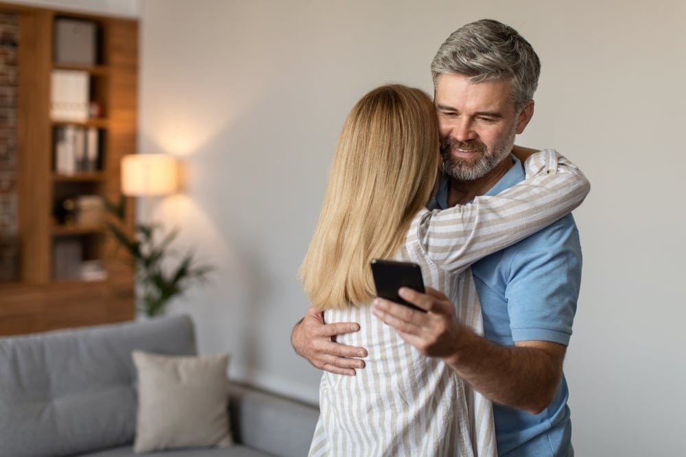 Man looking at his phone over his wife's shoulder.