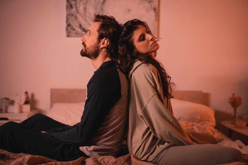 Man and wife sitting back to back in bed.