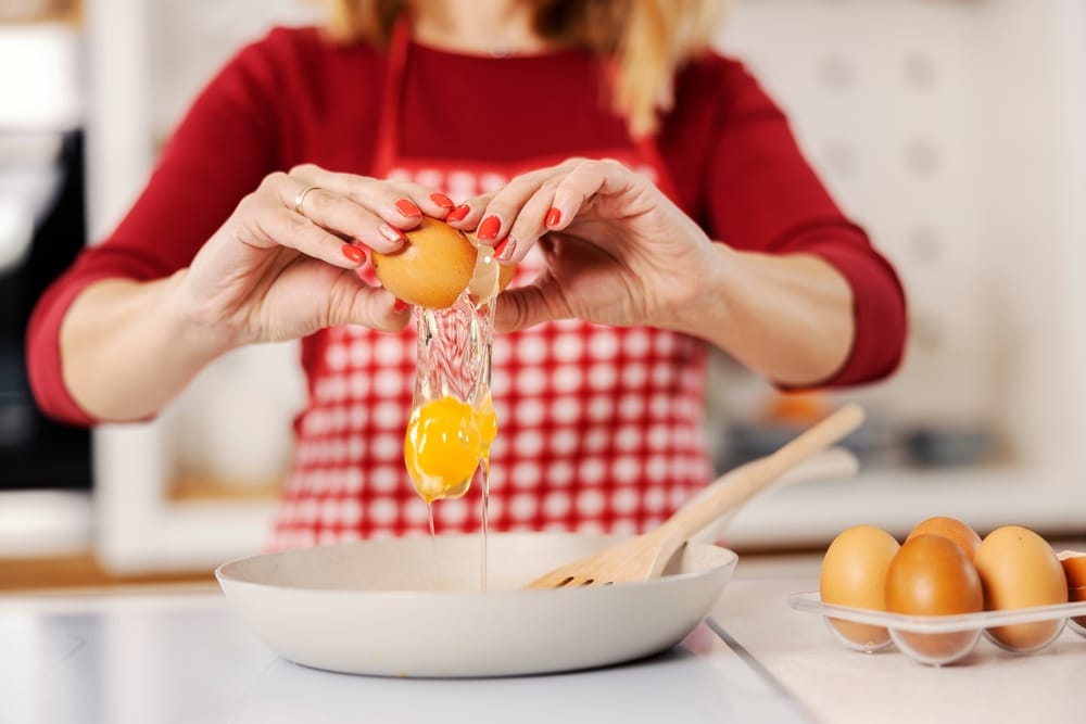 Woman in the kitchen cracking eggs.