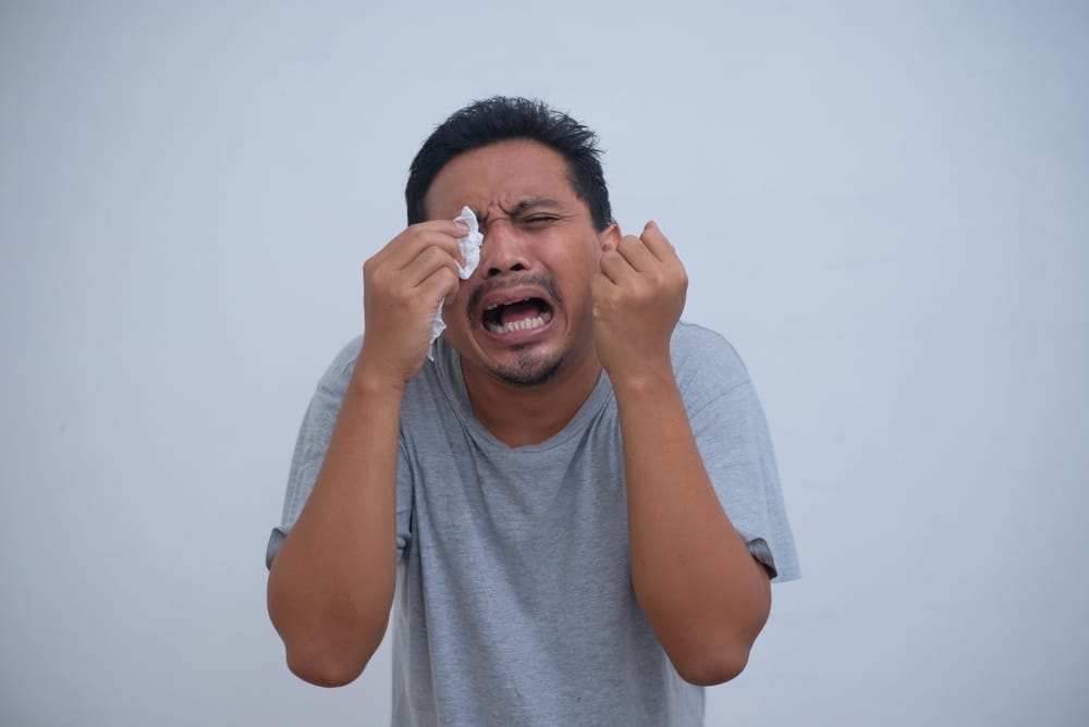 A man crying with a tissue at his eyes.