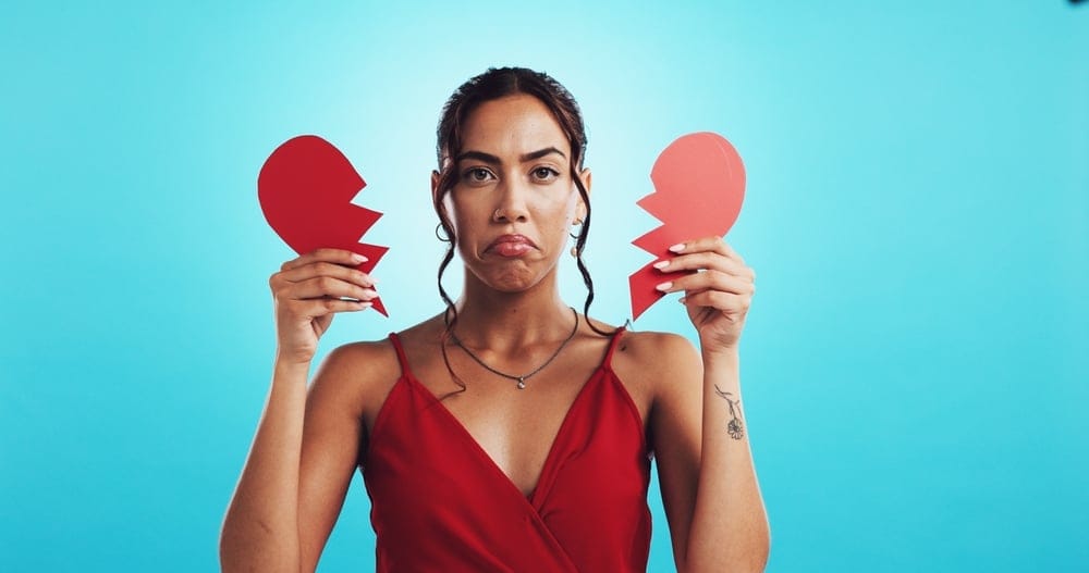 Woman holding a broken paper heart.