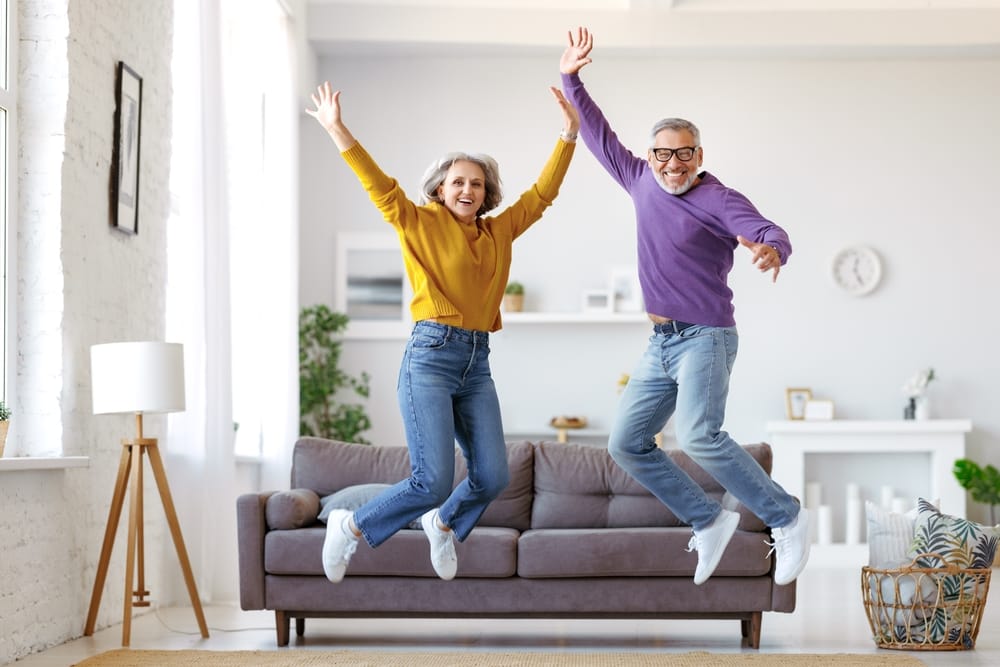 Happy active couple jumping in living room.