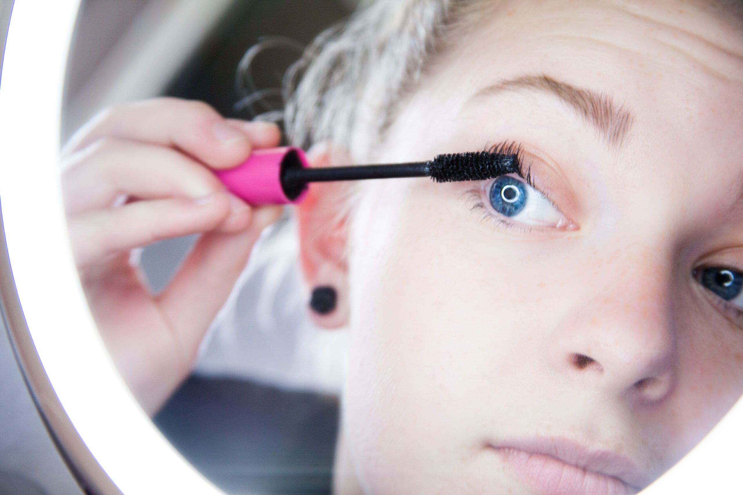 Woman applying mascara in the mirror. 