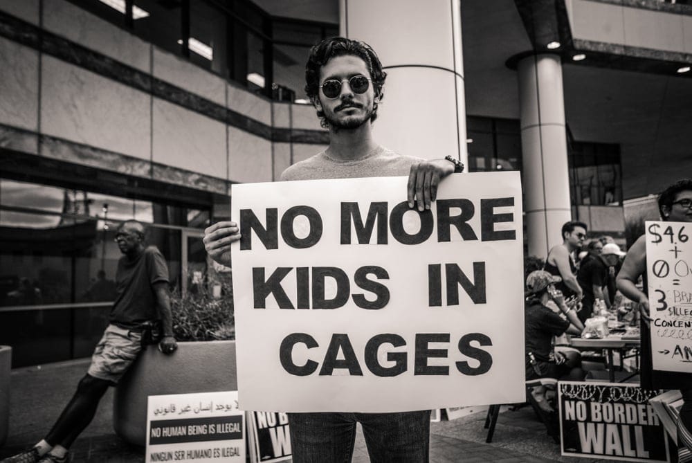 Male protester holding poster saying " No More Kids in cages" in reference to ICE raids