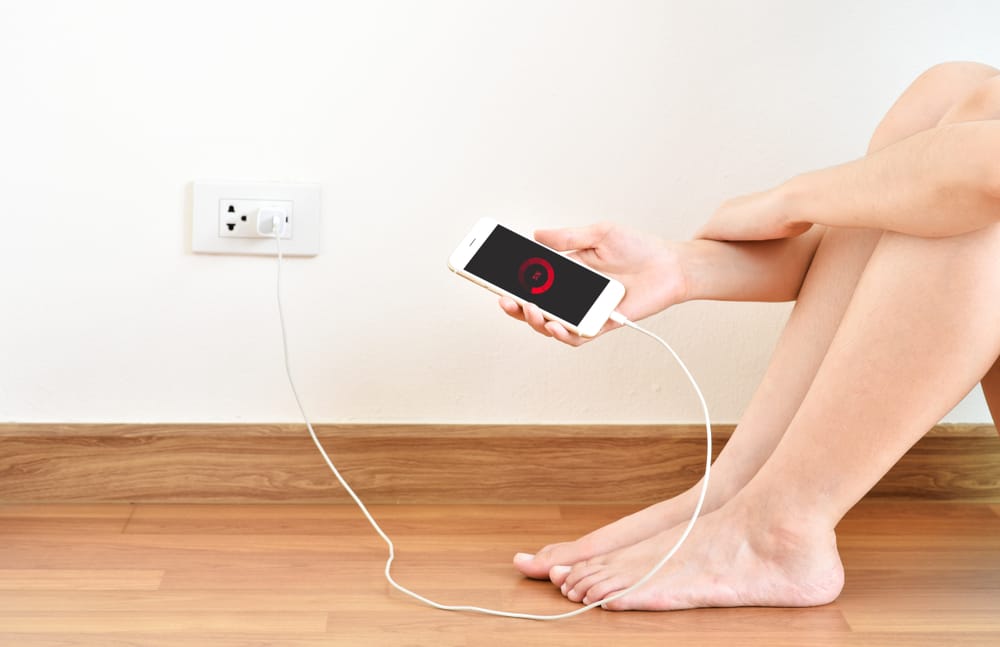 A young girl using her phone while charging it from a wall outlet