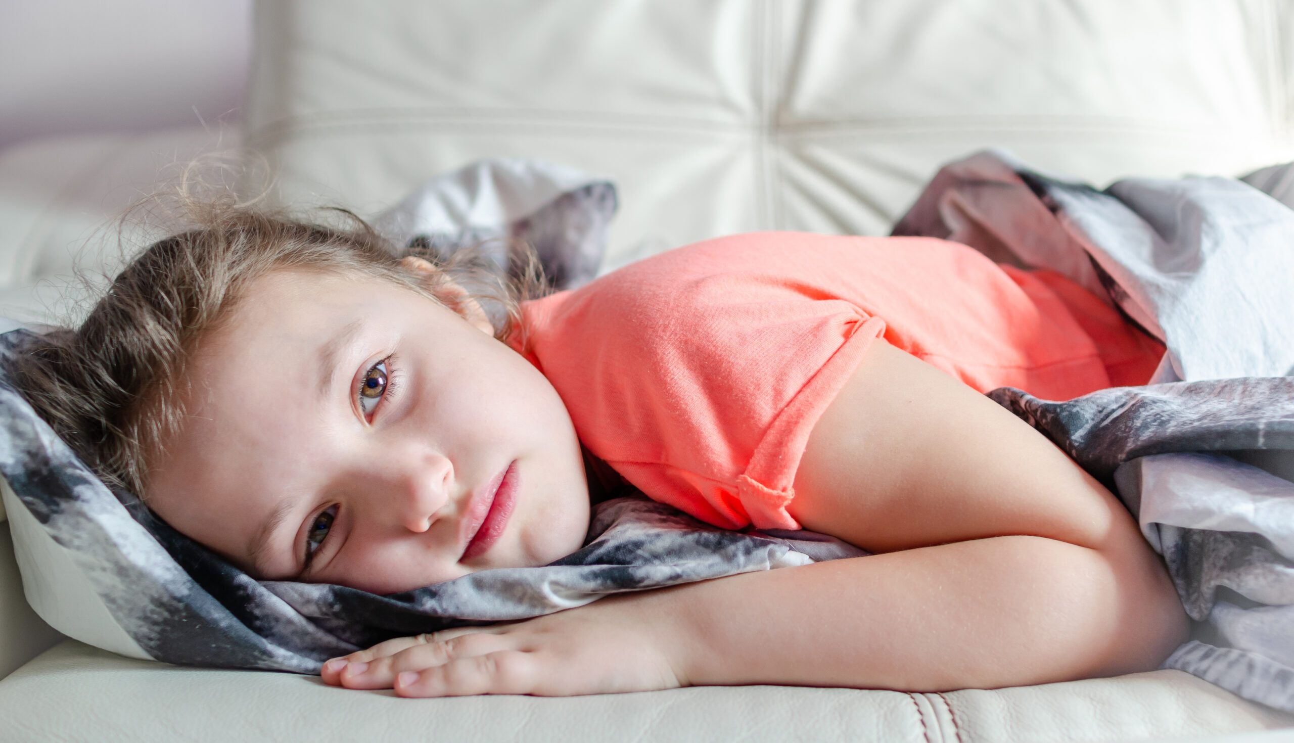An unhappy little girl laying alone in bed.