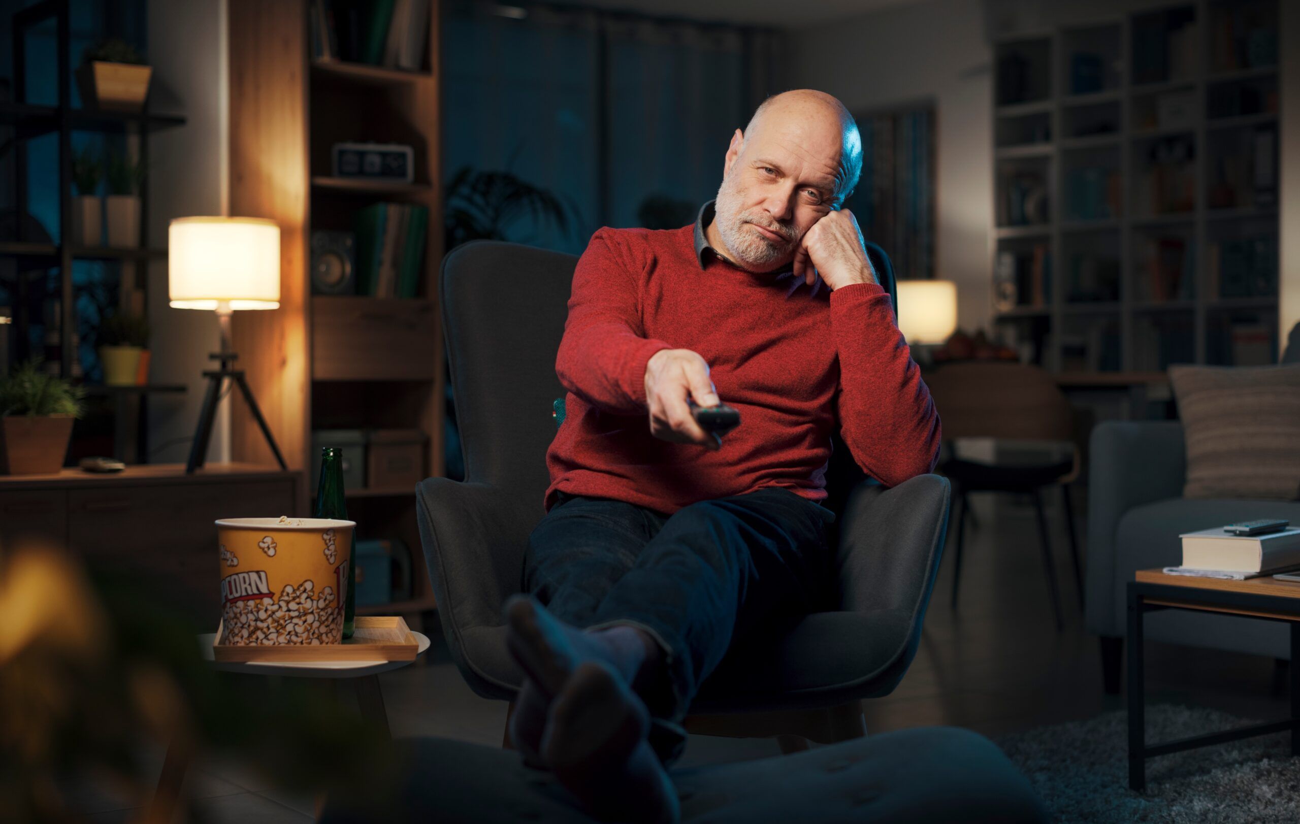 A retired older man watching TV alone in the dark.