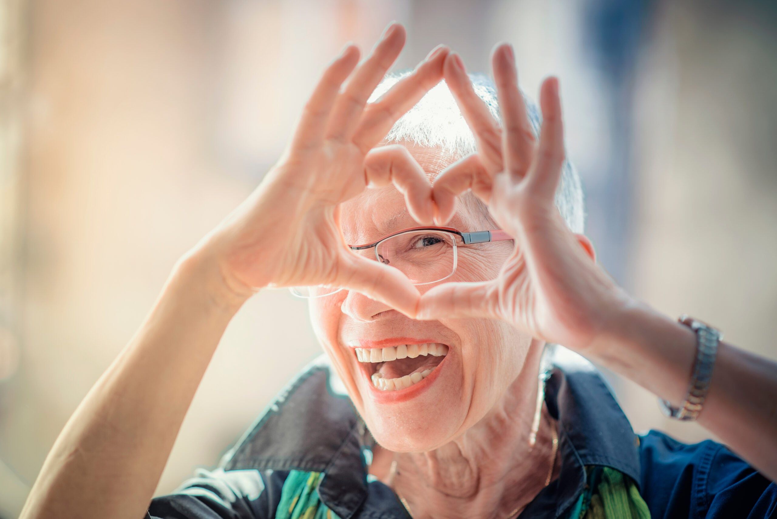 Senior woman making a heart shape with her hands and fingers while smiling.