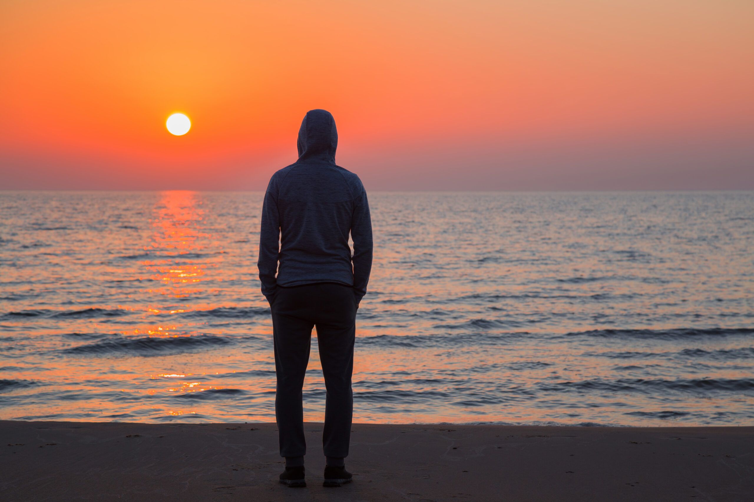 Man standing on beach looking at sunset alone.