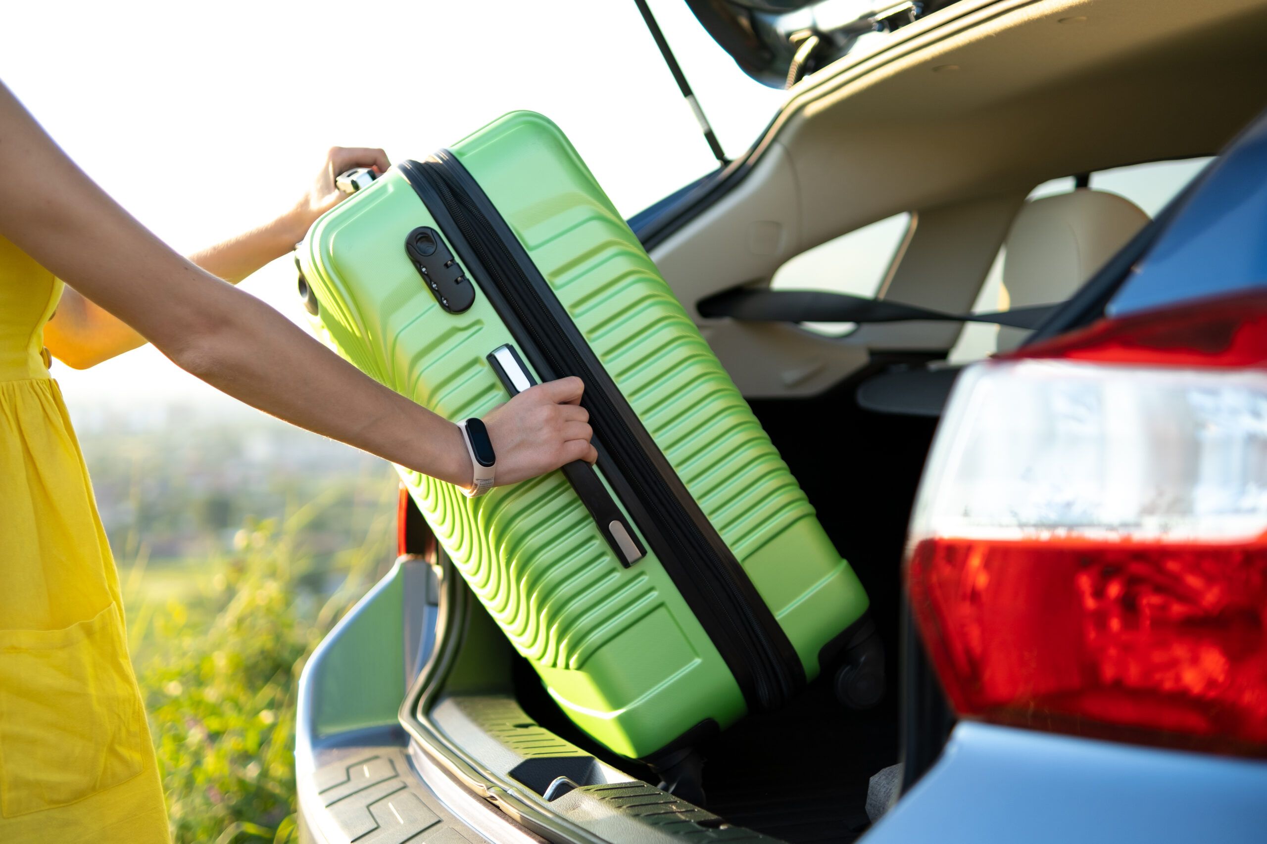 A woman packing her green suitcase into the car trunk.