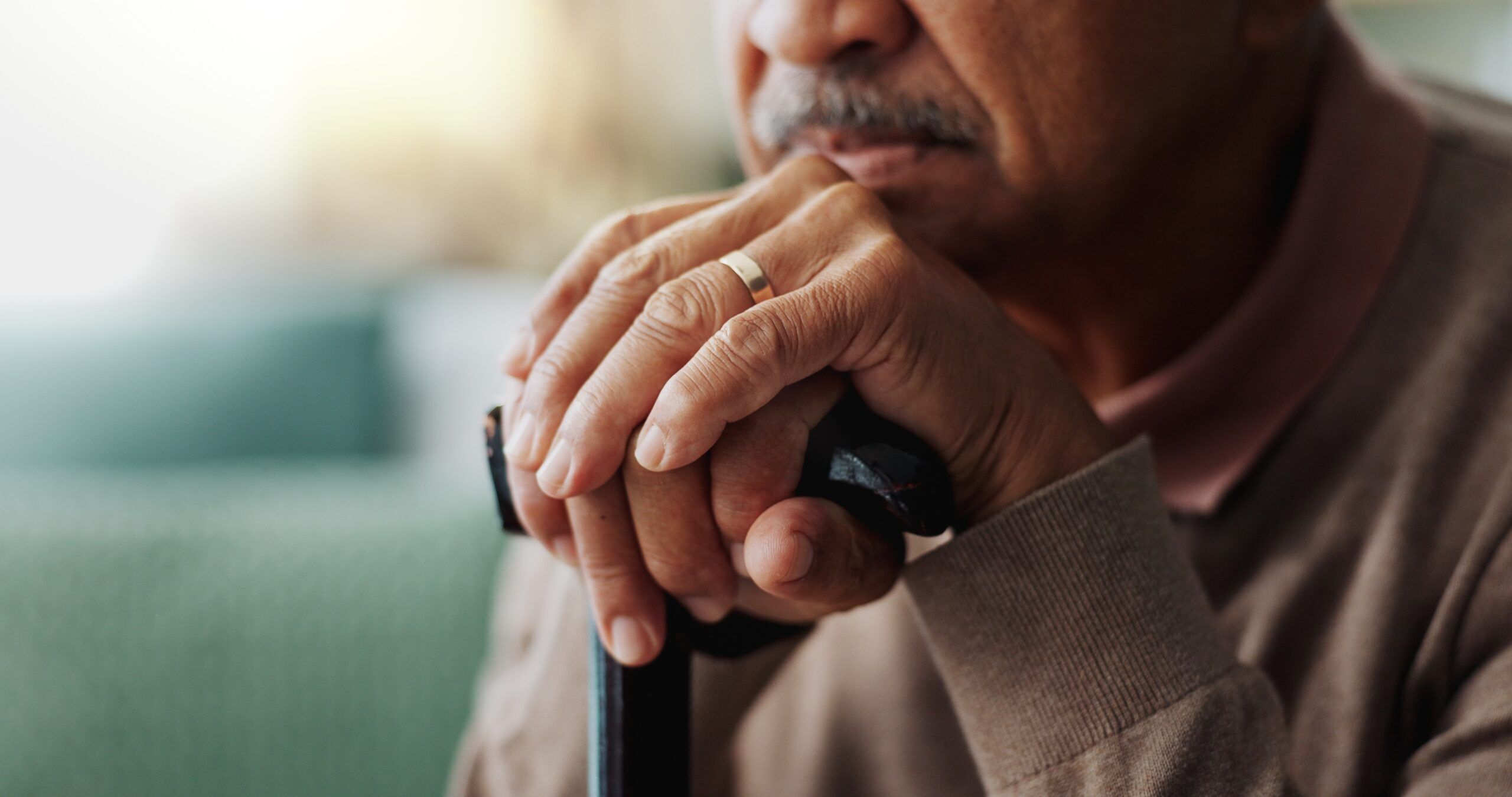 An old man with hands on his walking stick in a home for retirement.