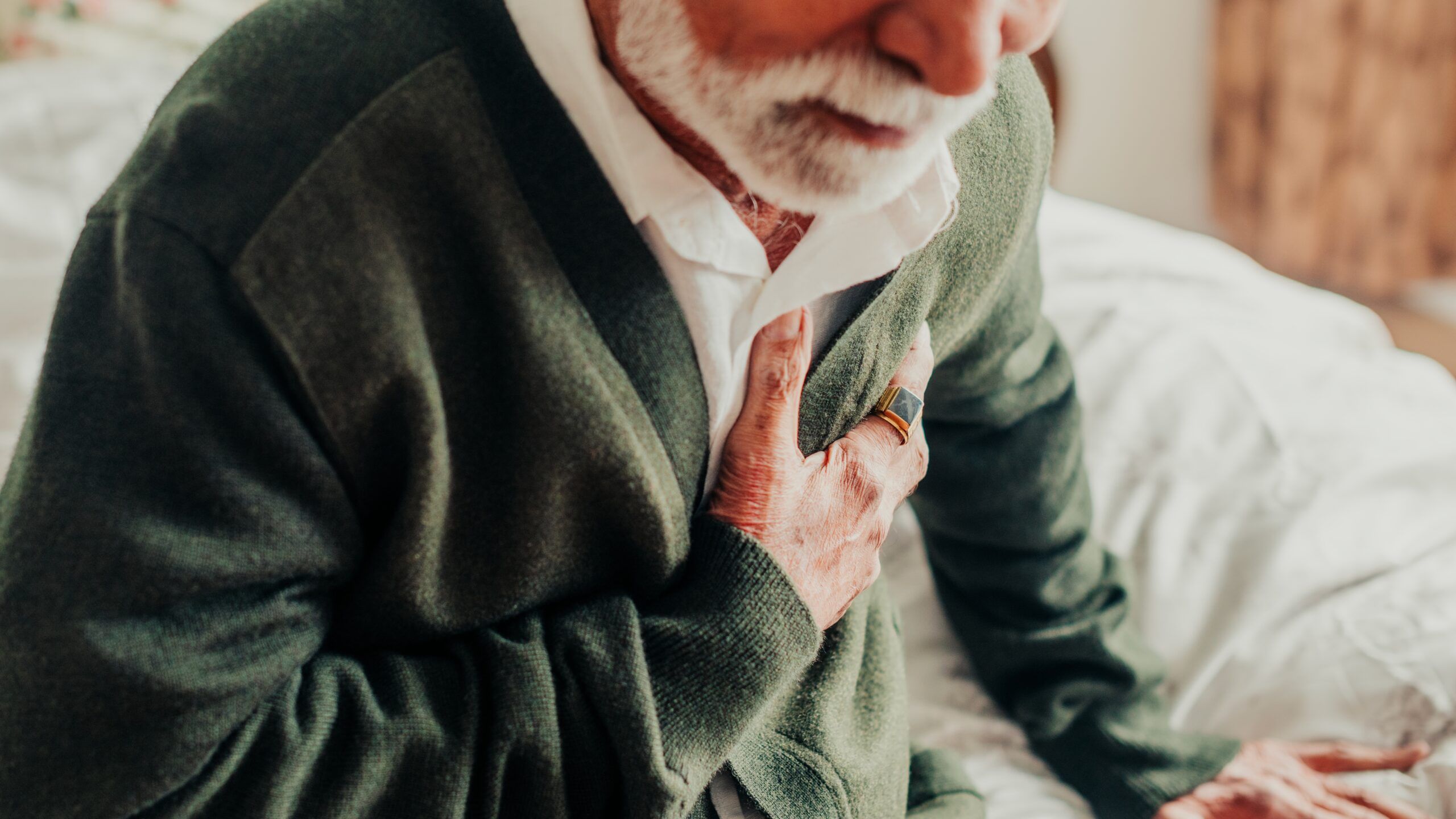 A senior man clutching at his chest getting out of bed.