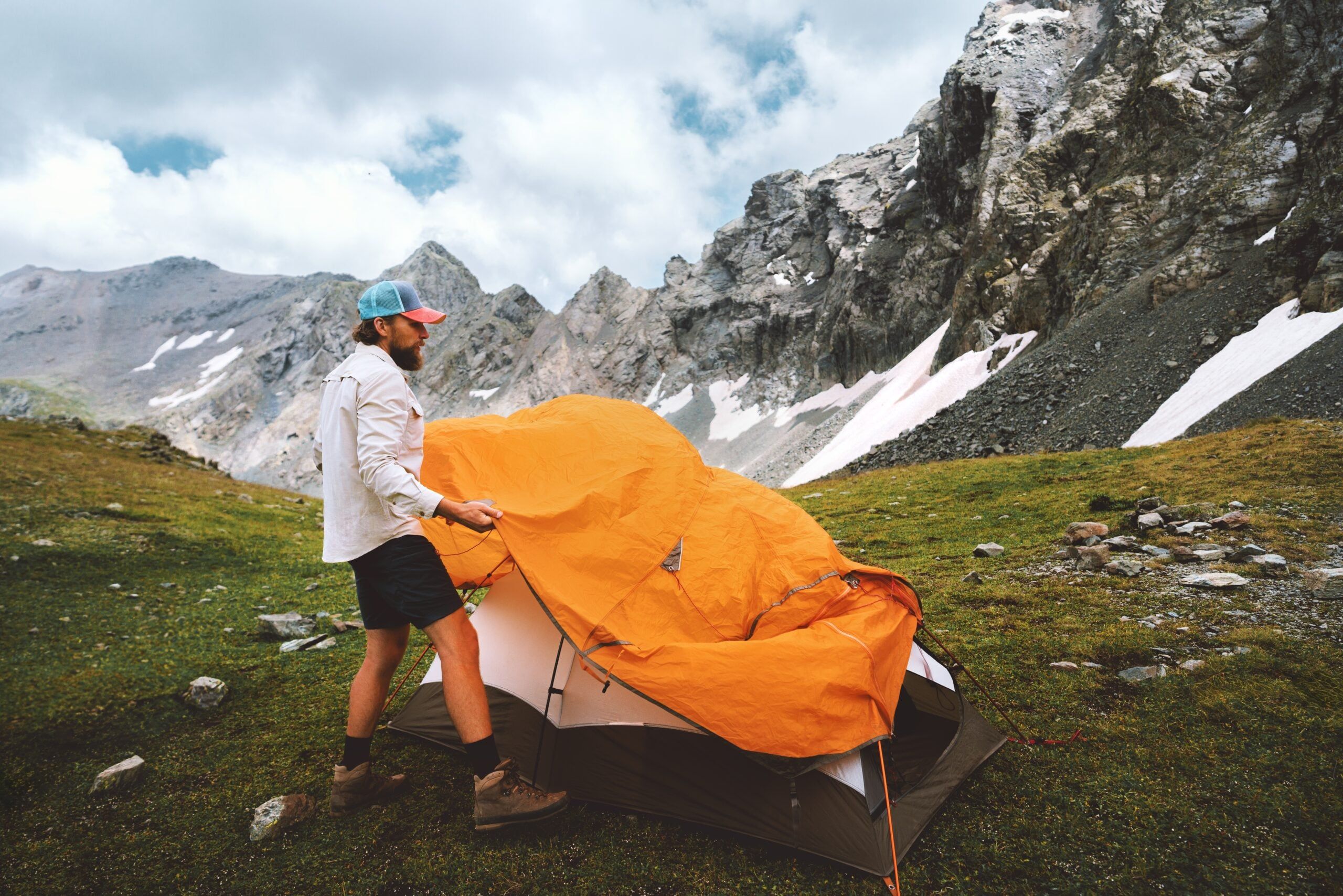 Man setting up a tent and camping gear in the mountains.