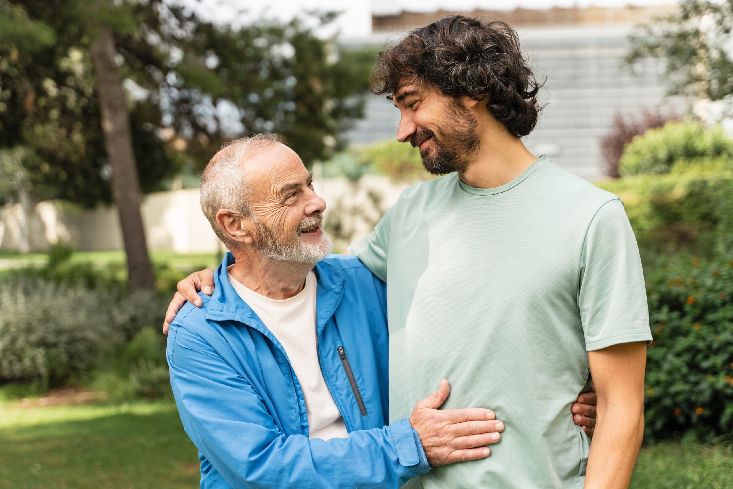 A senior dad and his adult son embracing outdoors.