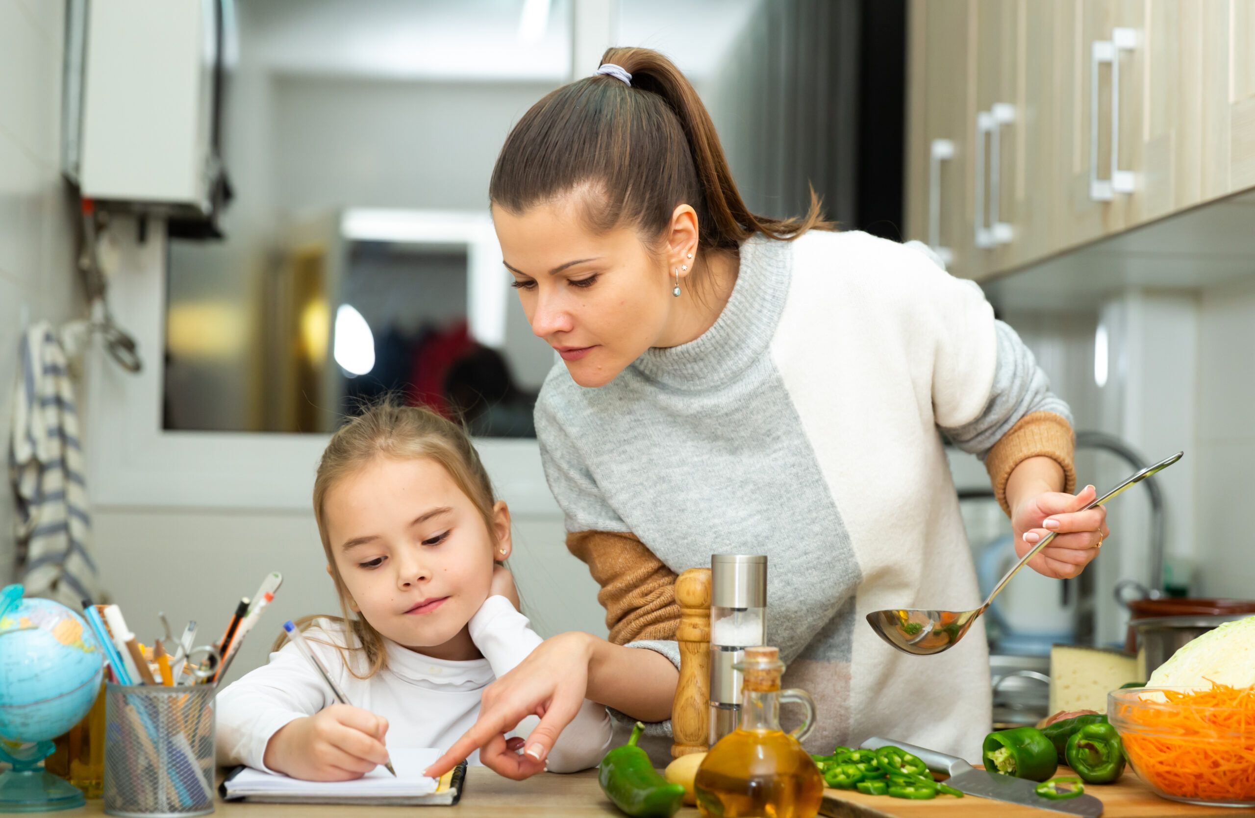 A busy mother making dinner and helping her daughter with schoolwork.