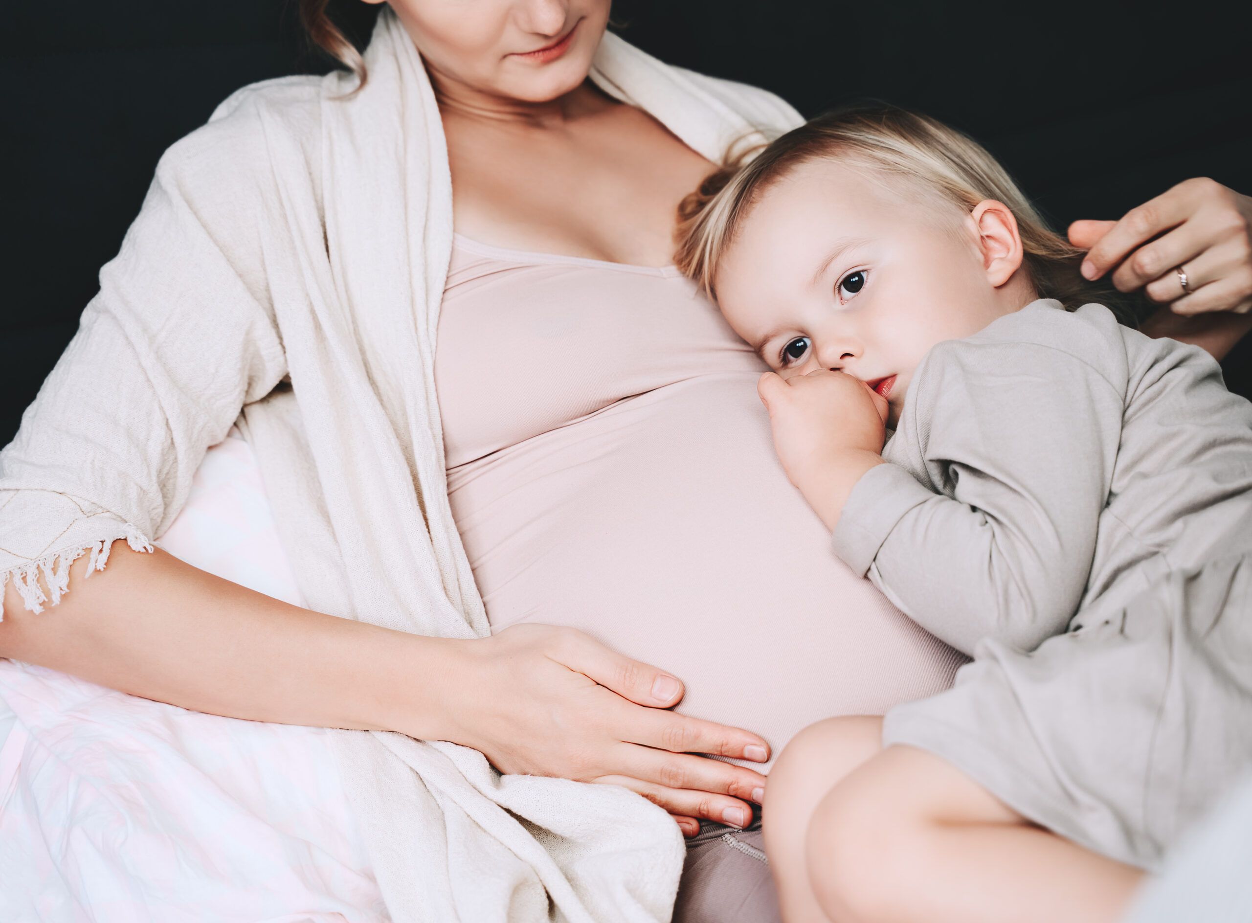 A pregnant mother with her toddler daughter laying in bed.