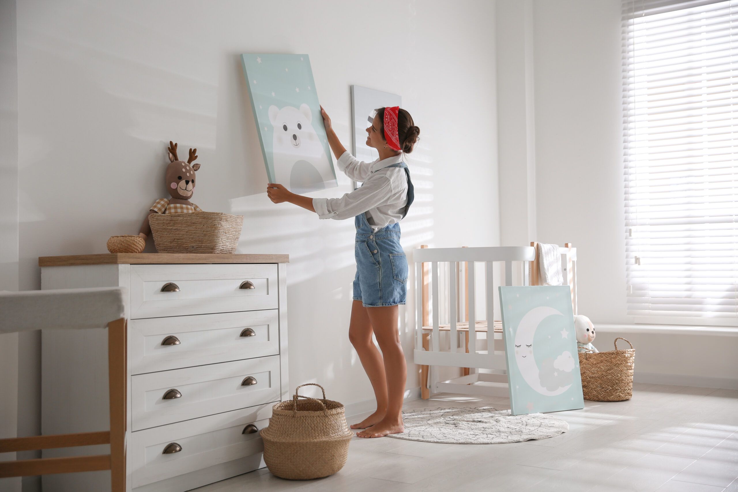 A woman hanging art in her baby's nursery.