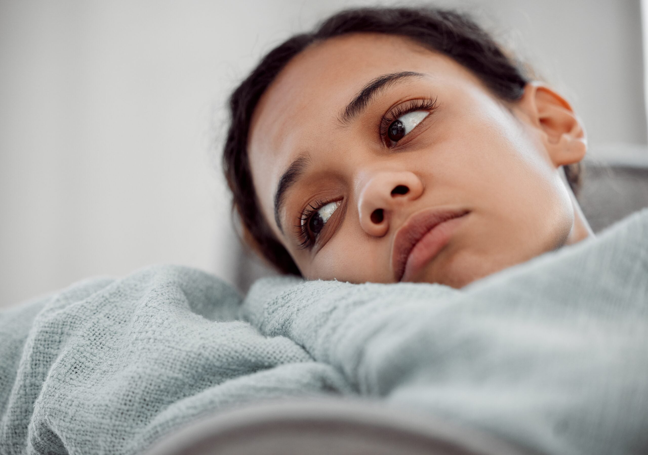 A young woman laying in bed feeling miserable.