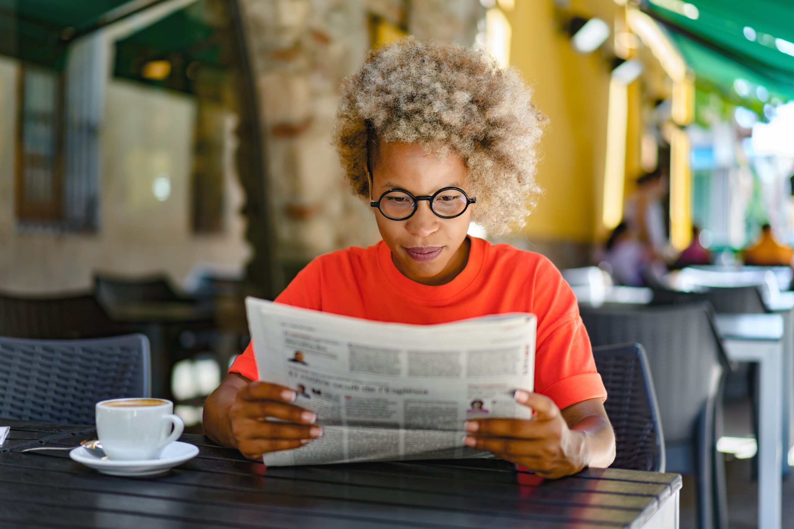 A woman reading the newspaper over coffee.