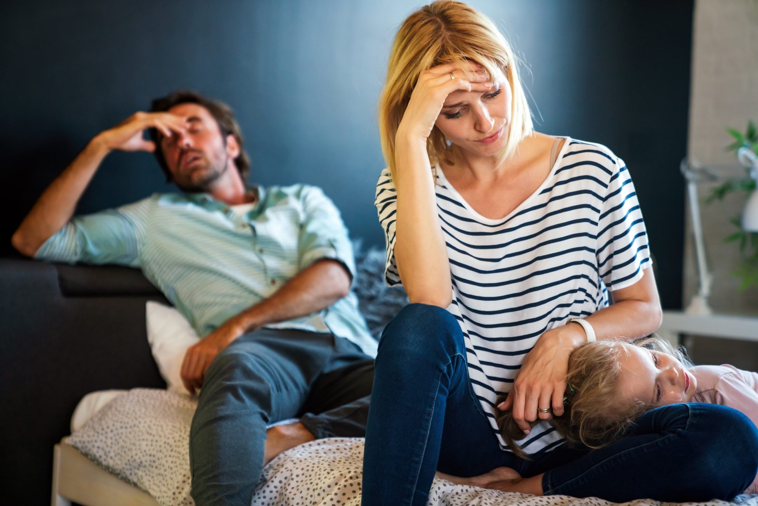An exhausted mother and father sitting on the couch with their young child.