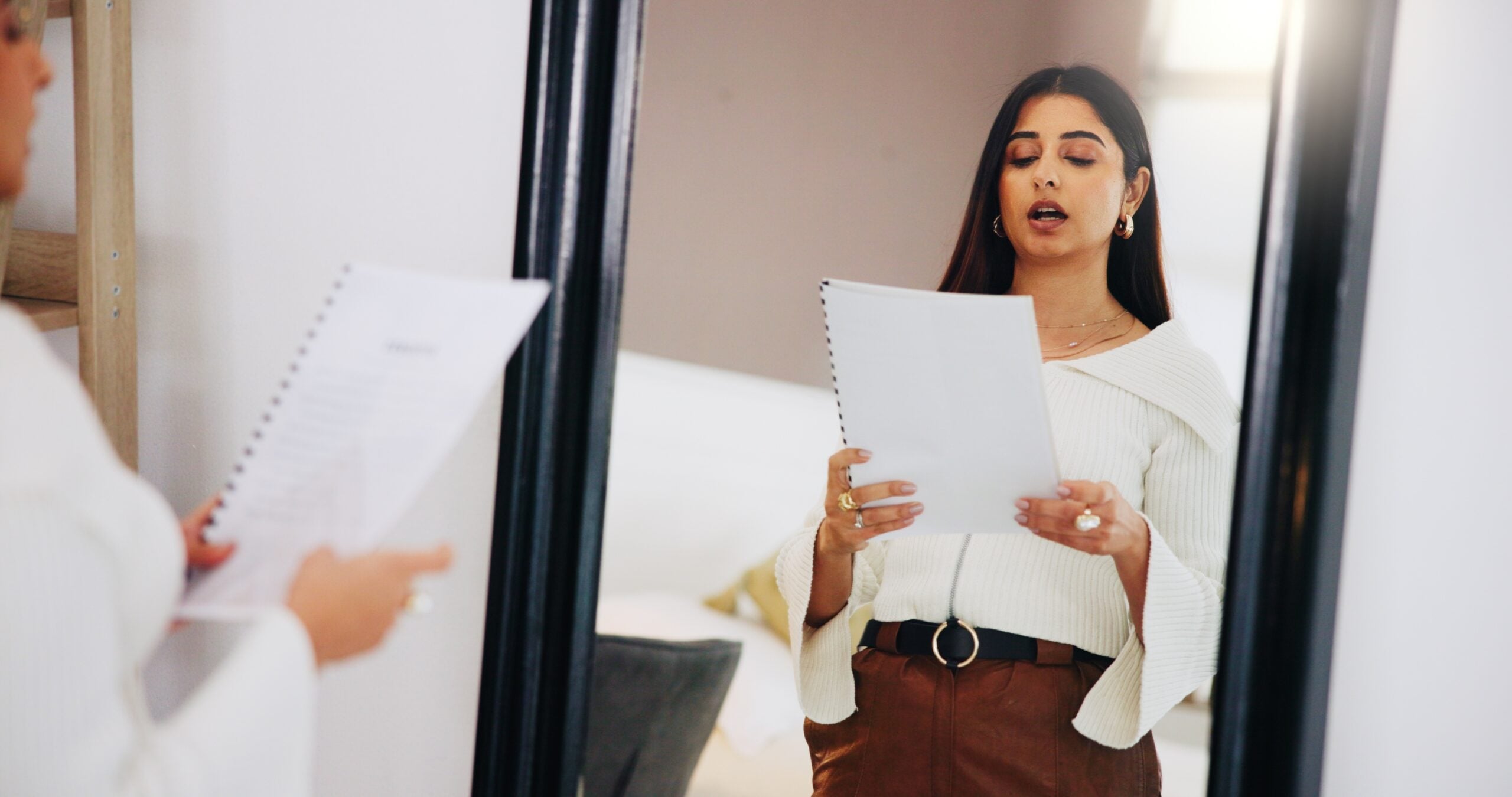 Nervous young woman rehearsing speech in front of a mirror.