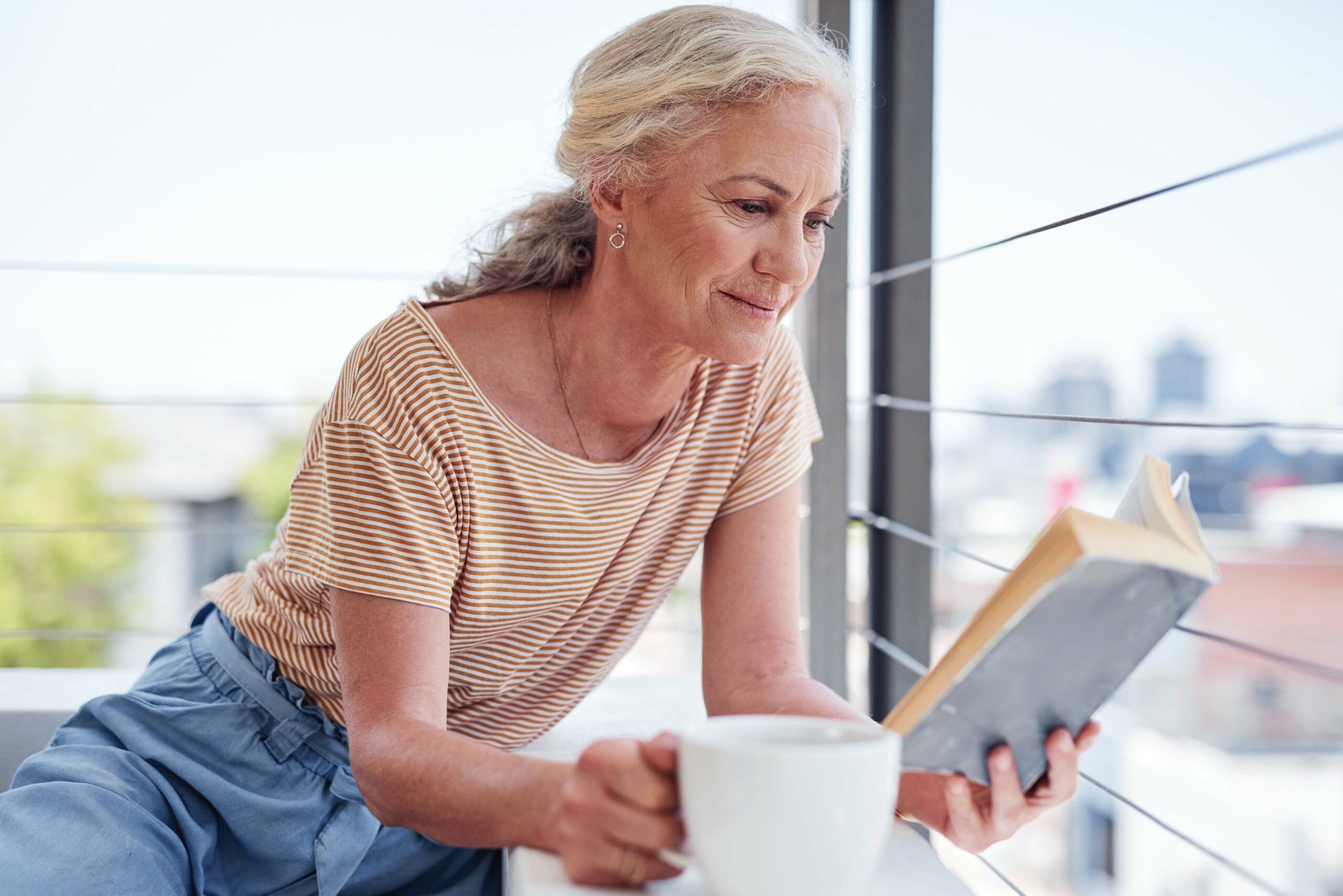 A senior woman reading a book and relaxing with coffee.
