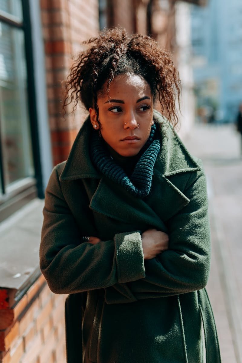Stylish woman in a green coat stands confidently on a city street, showcasing urban fashion.