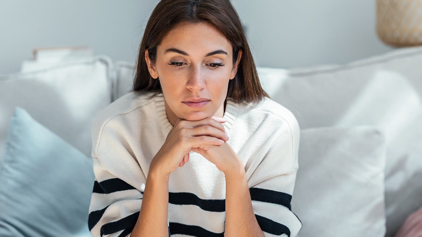 Shot of depressed young woman thinking about her problems while sitting on the sofa at home.