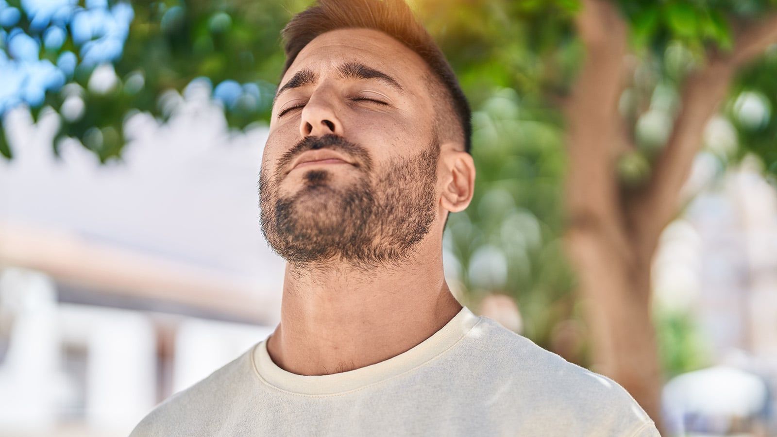 A man with short hair and a beard stands outside, eyes closed and head tilted up, appearing relaxed—a serene contrast to a scattered mind or an open browser tab. Green leaves and sunlight blur softly in the background, echoing Seneca’s wisdom on stillness.