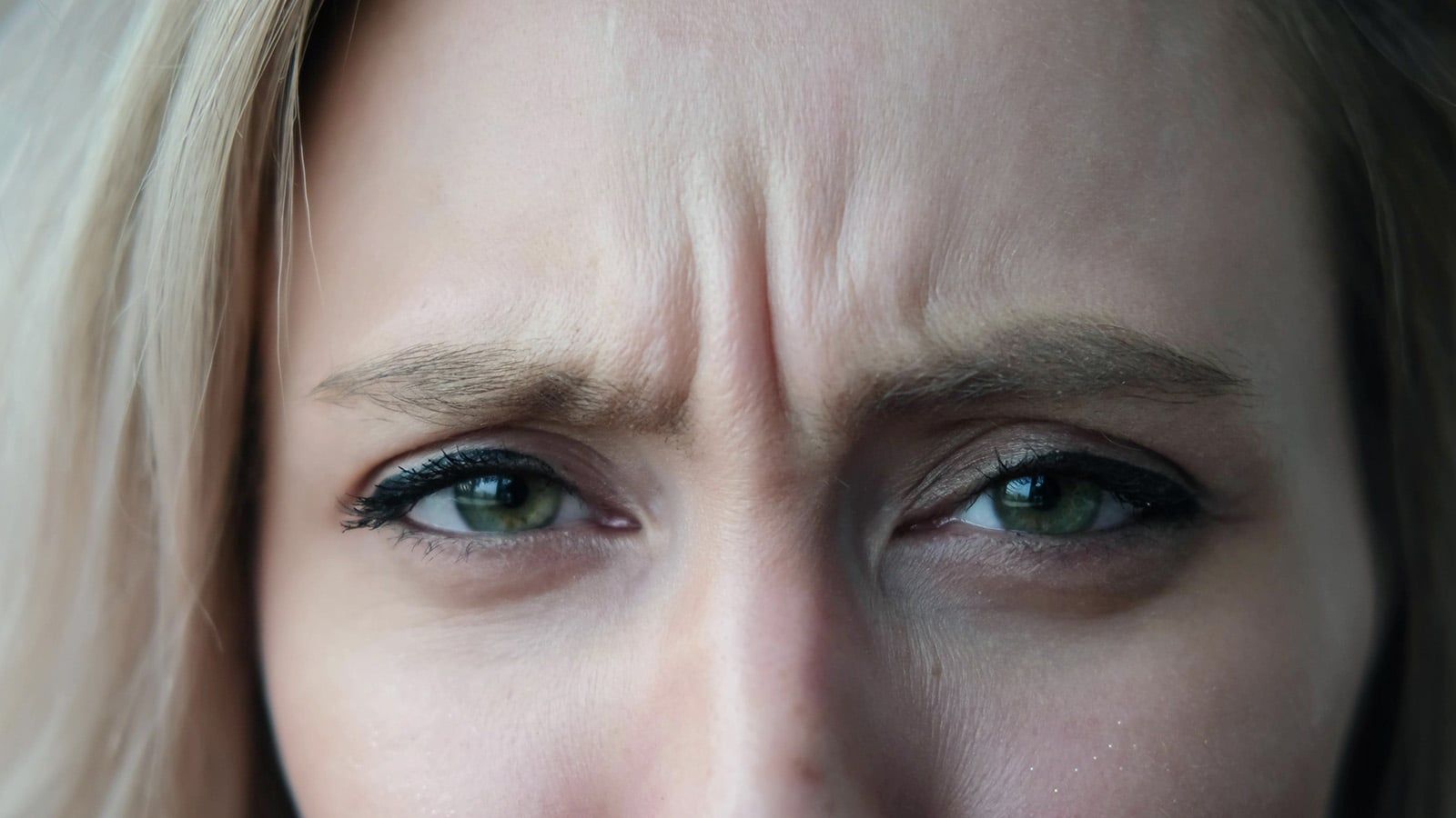 Close-up of a person's face showing furrowed brows and green eyes, with visible wrinkles between the eyebrows, suggesting a tired or concerned expression.