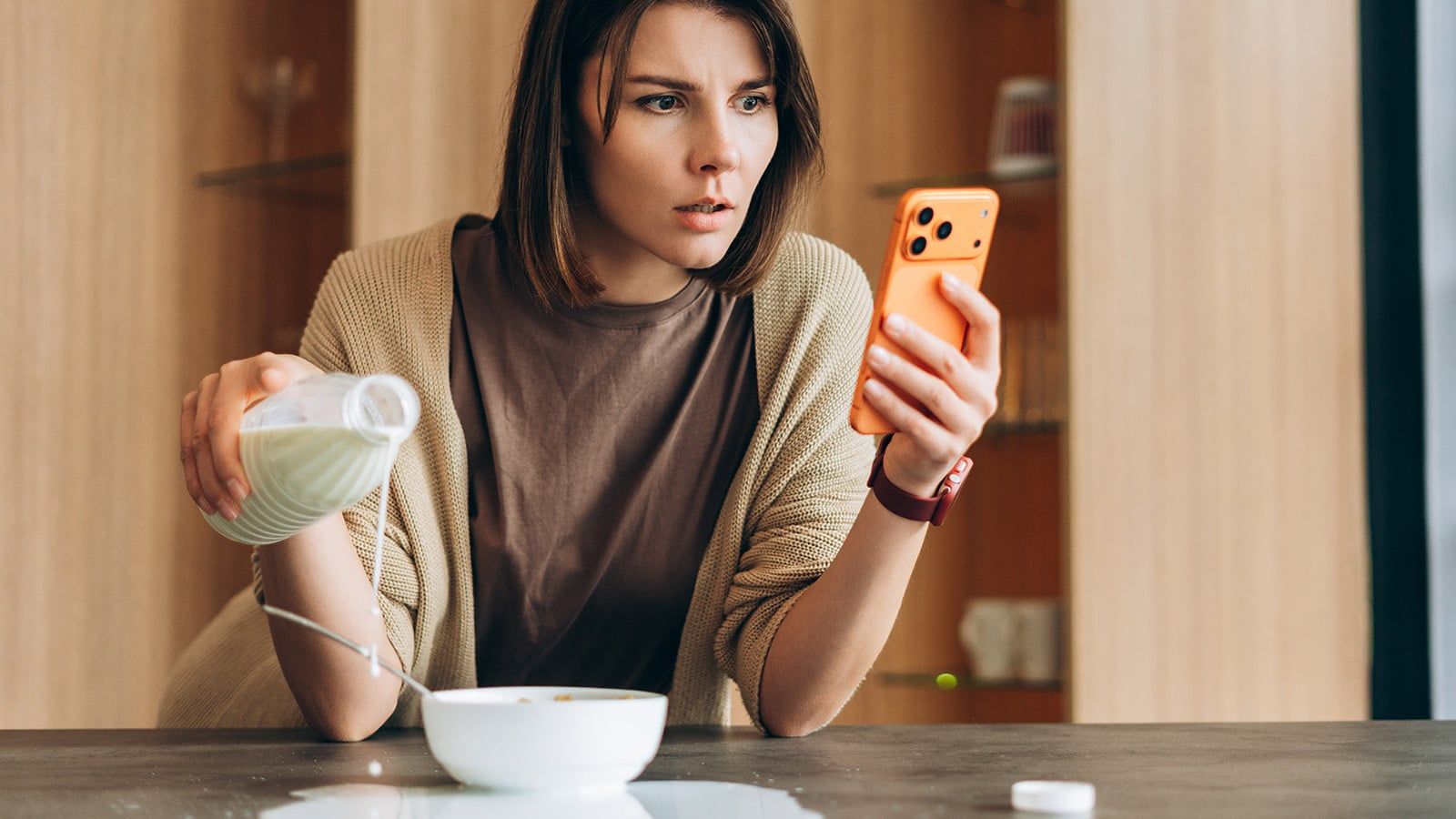 A woman with ADHD looks concerned at her smartphone, accidentally pouring milk over the edge of a bowl—highlighting how distractions can impact even simple tasks despite her intuitive reasoning.