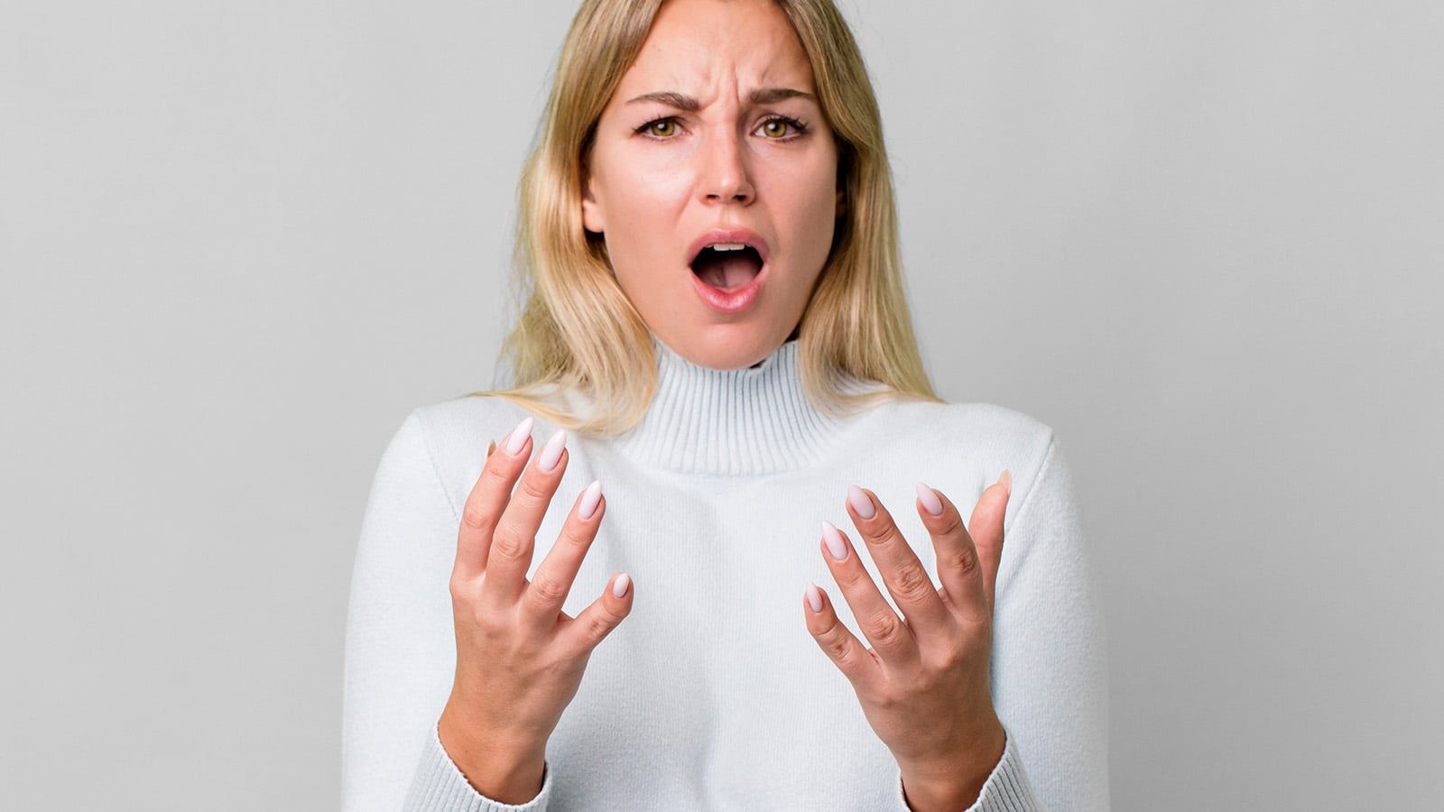 A woman with long blonde hair wearing a white sweater looks surprised or upset, possibly experiencing decision fatigue, with her mouth open and hands raised in front of her against a plain light background.