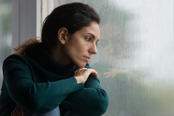 Woman alone looking out a window appearing sad.