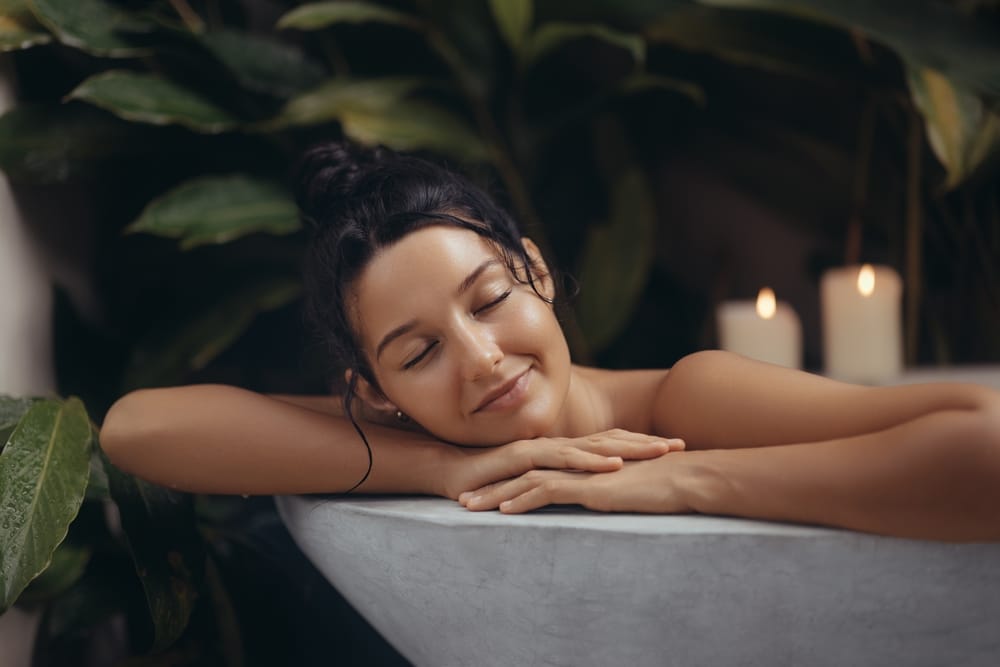 A serene young woman having a soak in her bathtub, she has a relaxed expression on her face