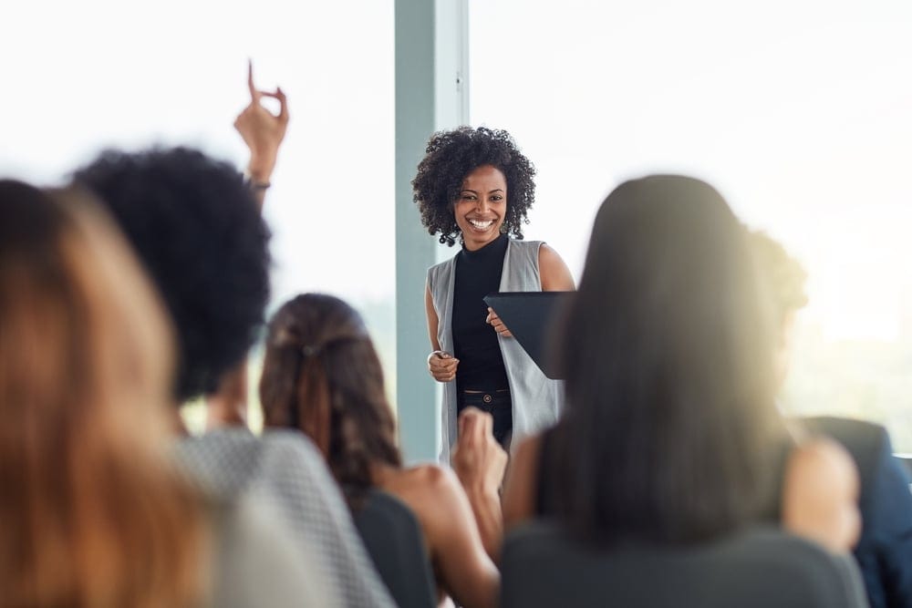 A black woman is being asked a question from someone in the audience with a raised hand