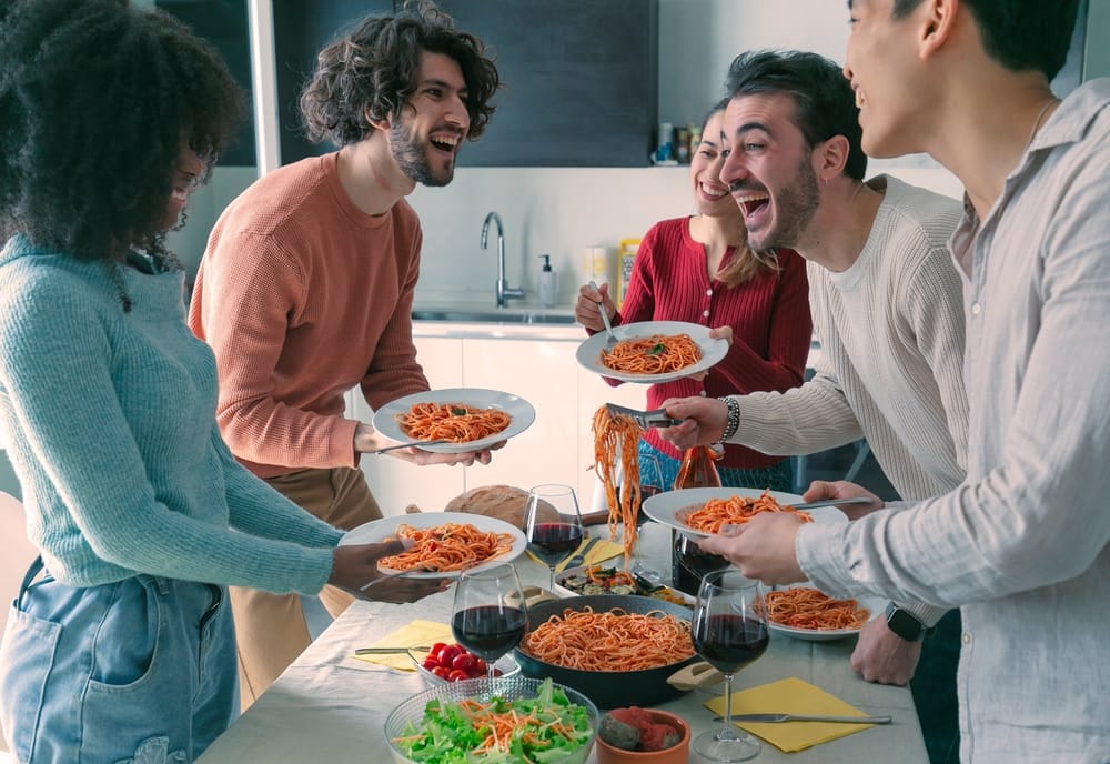 A group of friends having dinner together at home. The host, a man, is serving pasta to his friends