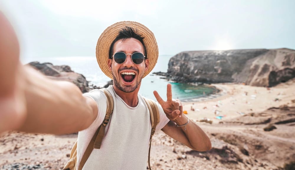 Man giving the peace sign with his fingers and standing at the beach.