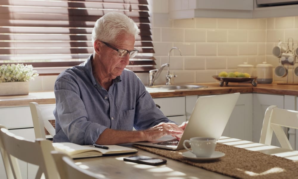 An elderly man working on his laptop in the kitchen