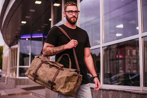 Bearded man in glasses with leather bag near evening city. tattooed man