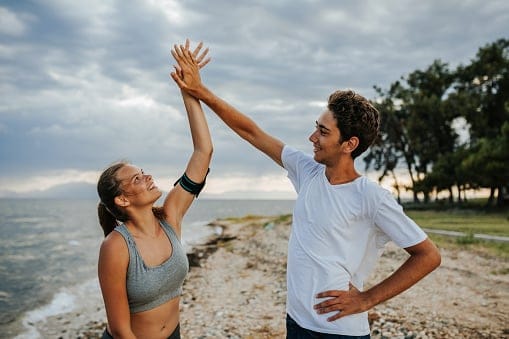 Beautiful young couple giving each other high five after hard training on the beach