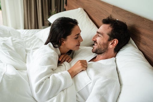 Smiling couple is lying in bed and looking at each other with love.