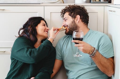 woman feeding boyfriend pizza and wine