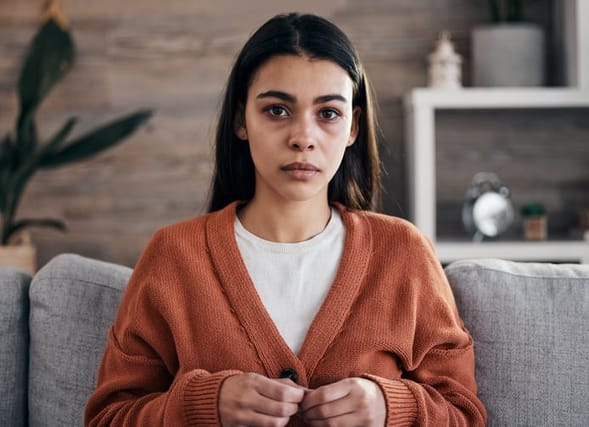 sad woman in orange cardigan on couch