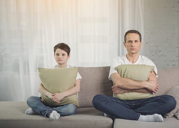 Portrait of resentful parent and child keeping silence. They are sitting on couch and hugging cushions with sadness