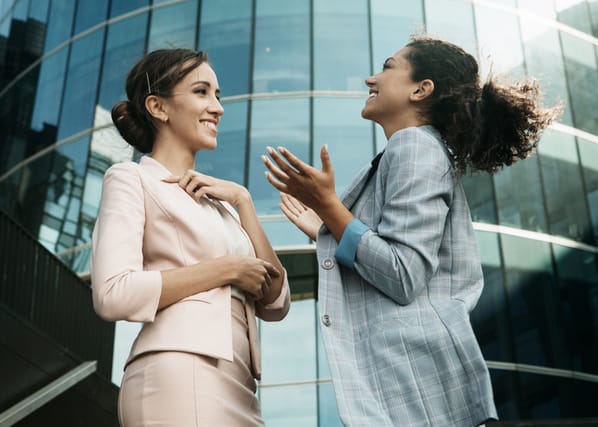 Two business women having a casual meeting or discussion near a modern office. Summer time.