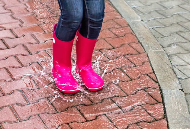 Autumn. Protection in the rain. Girl wearing pink rubber boots jumping into a puddle with splash. Street, city. Raindrops. Copy space. Place for message. Outdoor Concept about activity, leisure, travel.